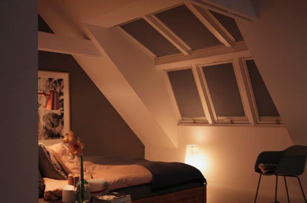 Ein Schlafzimmer, bei dem die Fenster mit geschlossenen Rollos komplett verdunkelt sind: Lichtquellen sind vor dem Schlafengehen zu minimieren | VELUX Magazin.