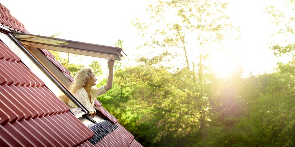 Une femme regarde la verdure par sa fenêtre de toit et fait le plein de lumière du jour | Magazine VELUX